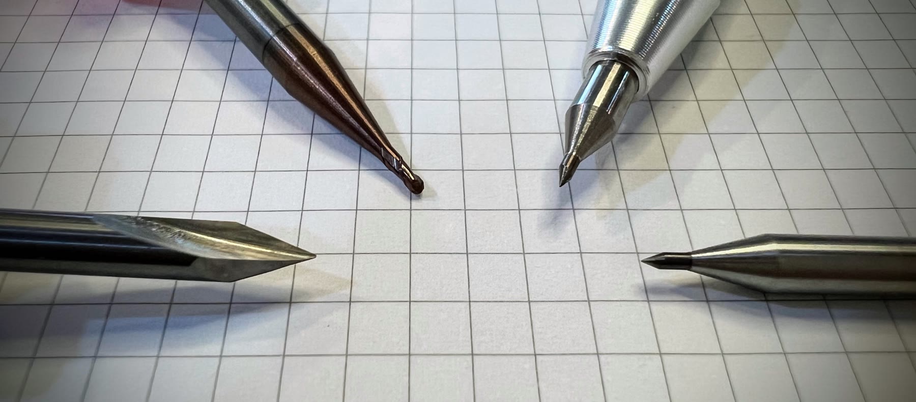 A micro end mill, V-bit, and several carbide scriber tips arranged together.