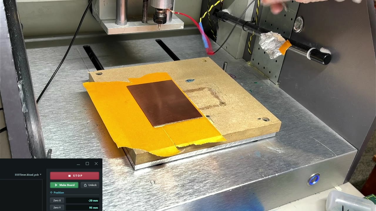 A copper-clad blank mounted flat on painter's tape on the CNC wasteboard.